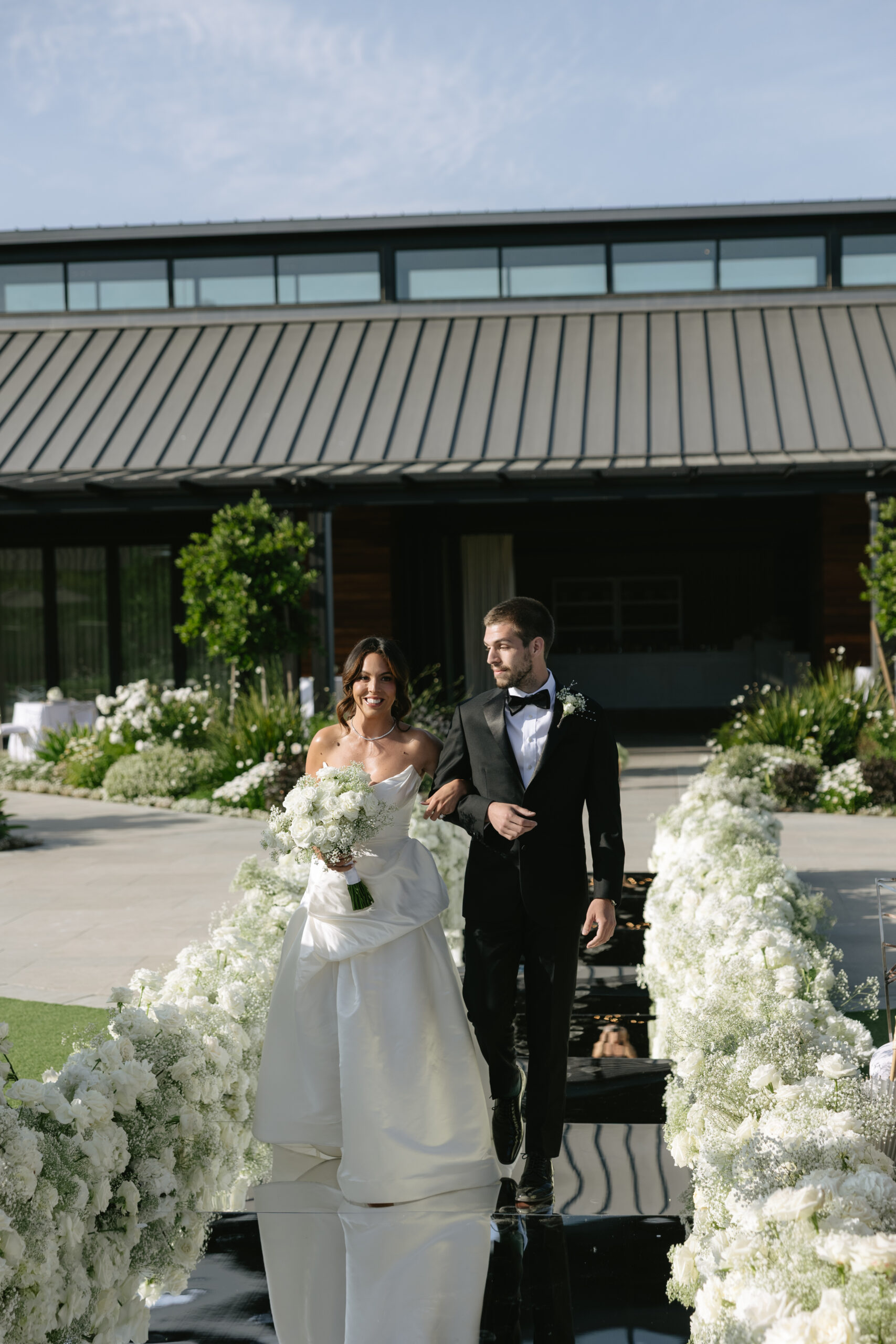 Bride being walked down the mirror floral lined aisle