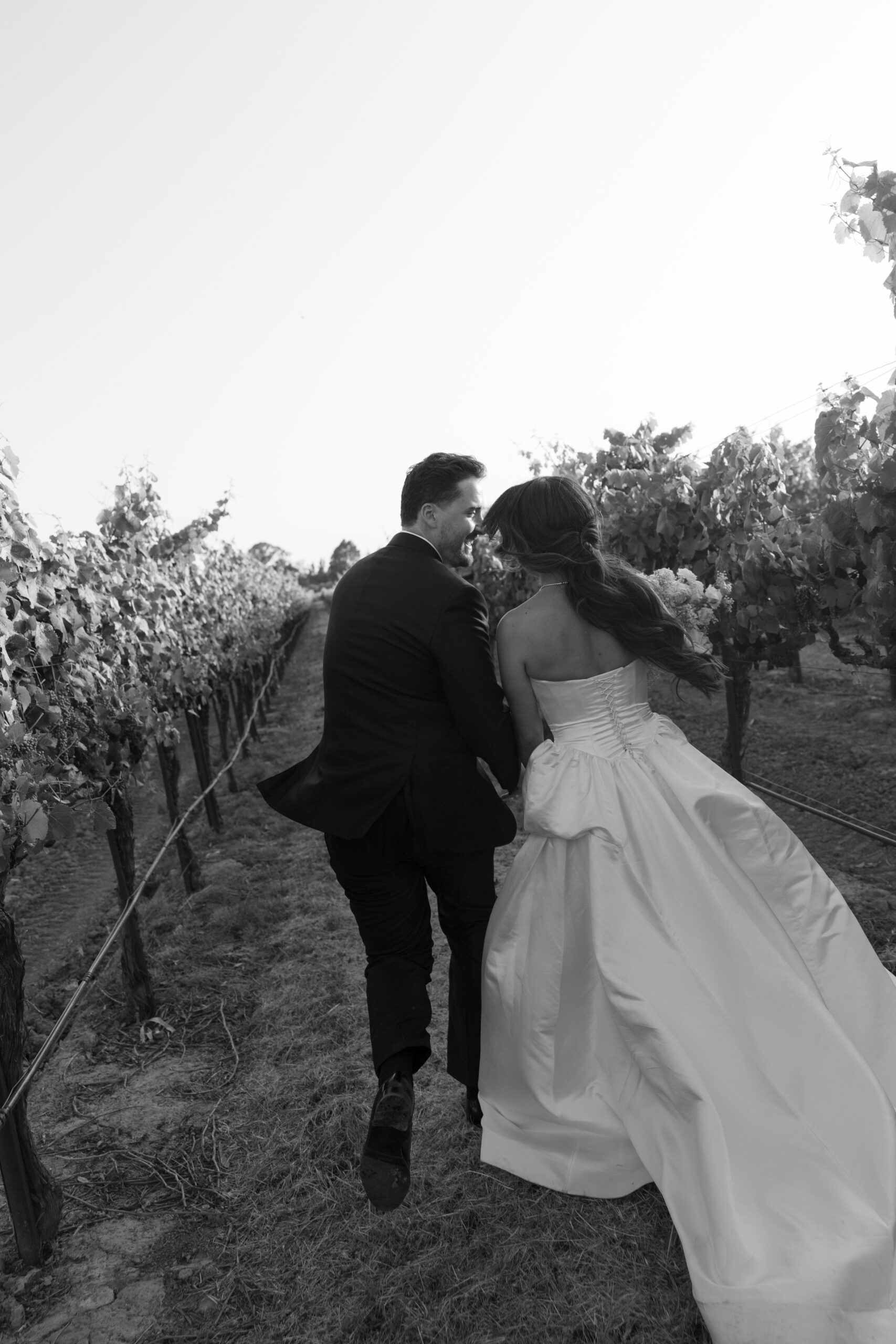 Black and white wedding photo of bride and groom running through the vineyards at Stanly Ranch