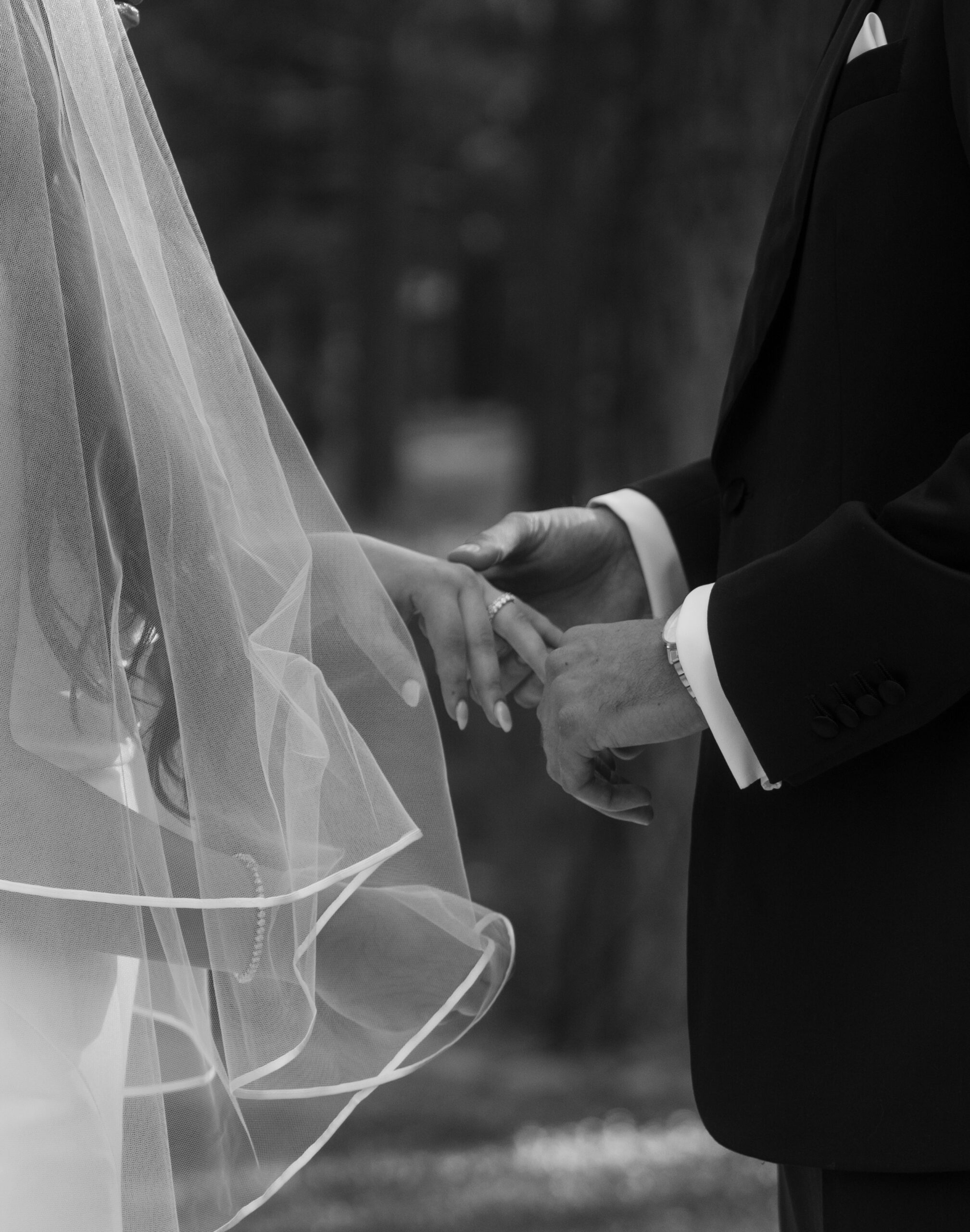 Black and white photo of groom putting ring on bride's finger during ceremony