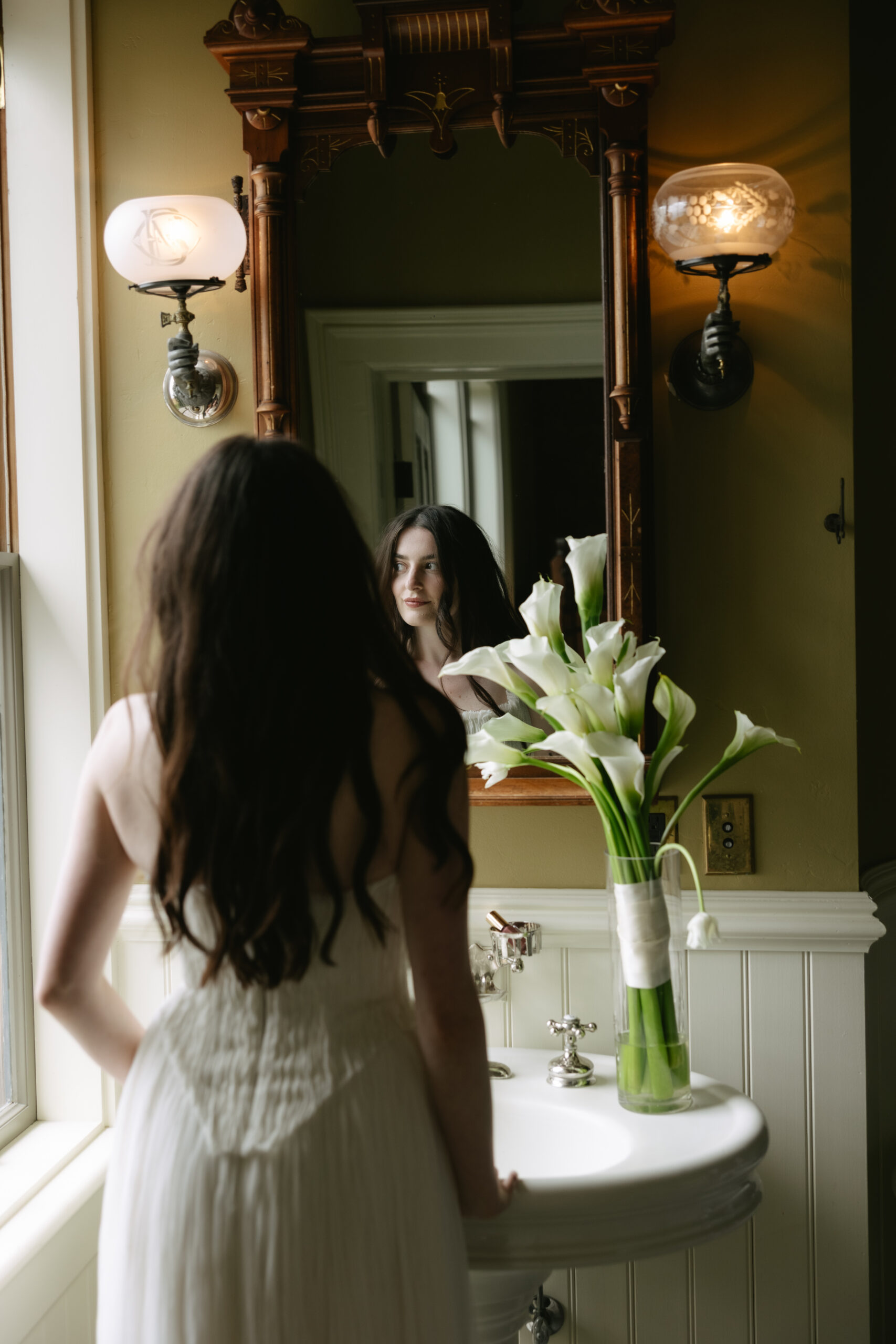 Bride getting ready for her wedding in the mirror with a calla lily bouquet