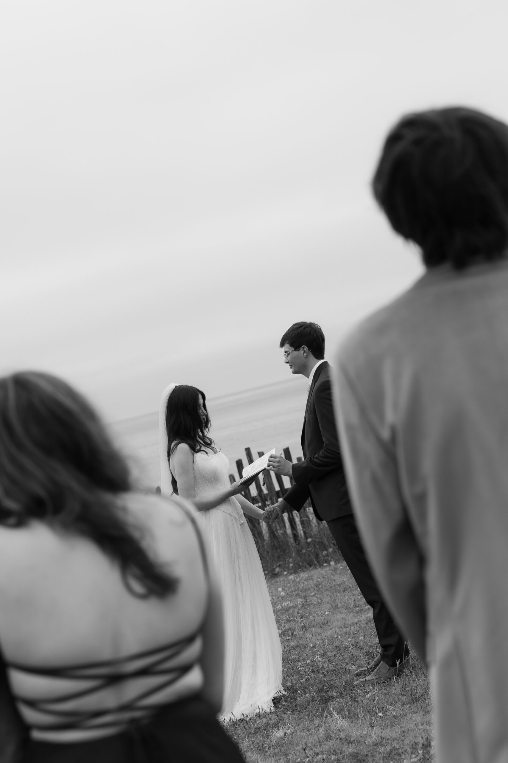 Black and white photo of bride and groom saying vows framed between wedding guests