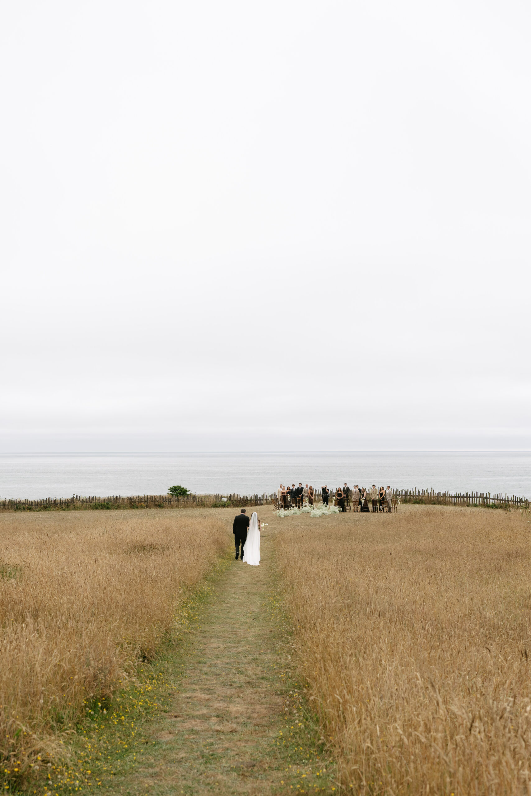 A bride being walked through a meadow to her wedding ceremony