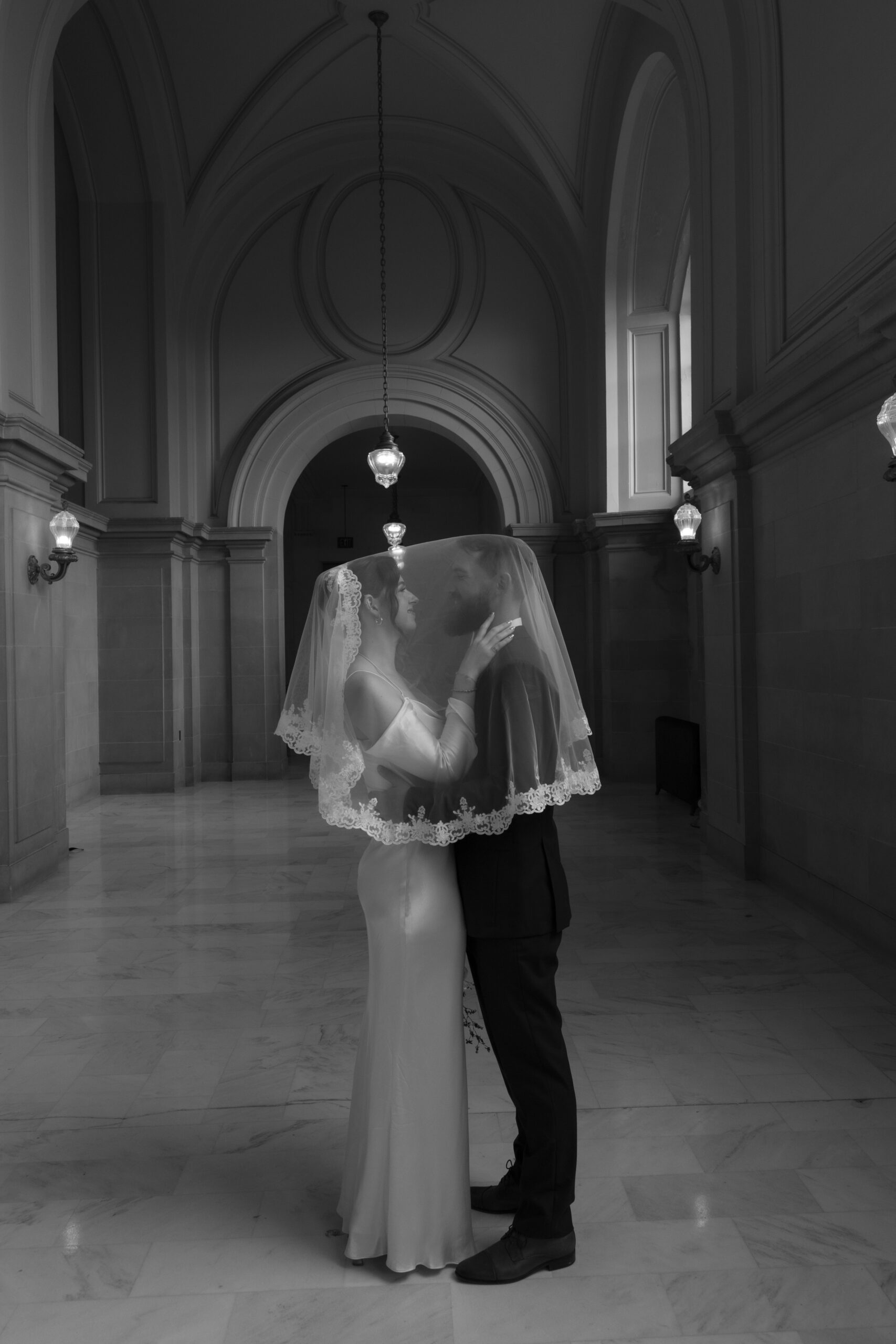Bride and groom posing in a San Francisco City Hall hallway under a veil