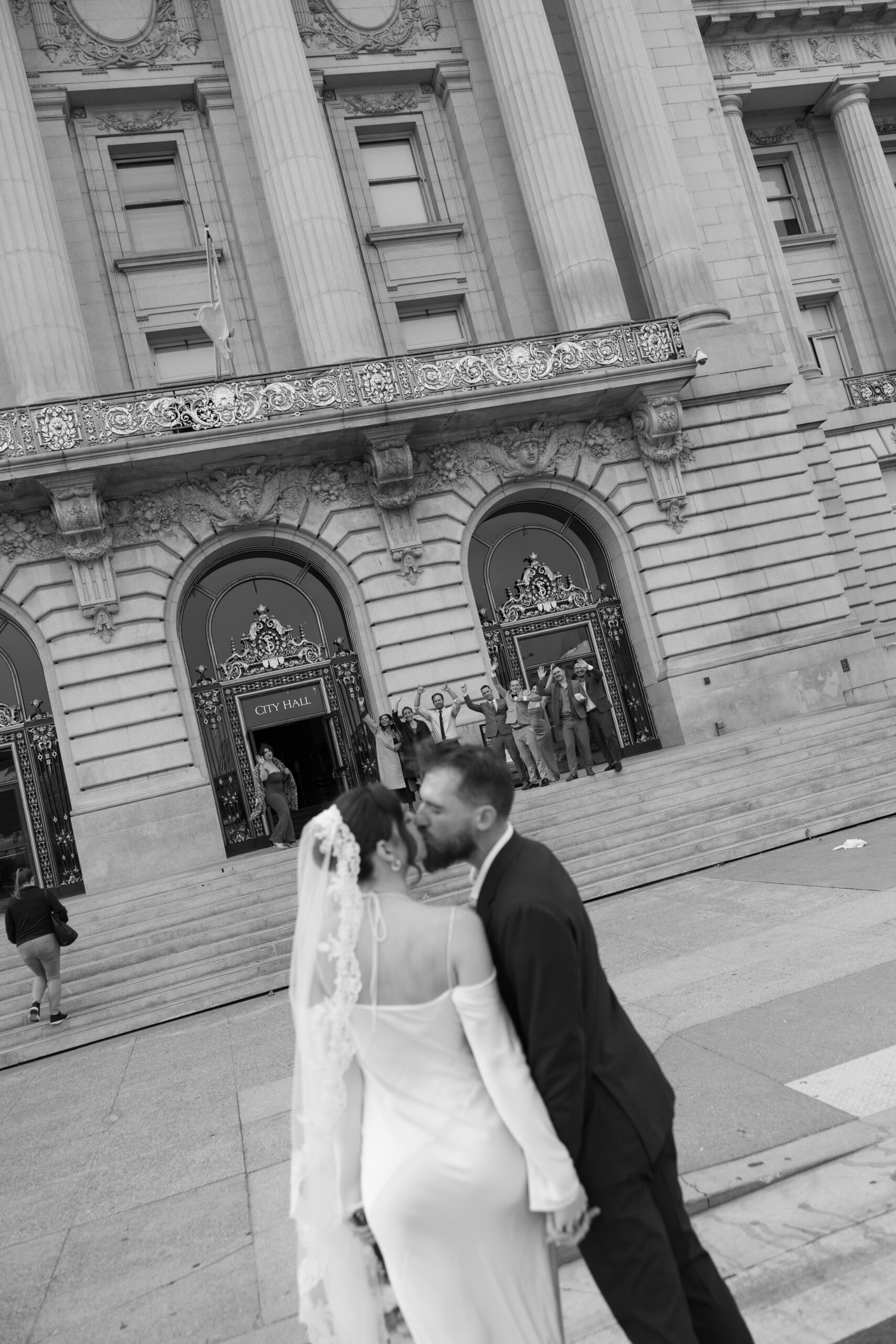 A black and white photo of a bride and groom kissing in front of the San Francisco City Hall