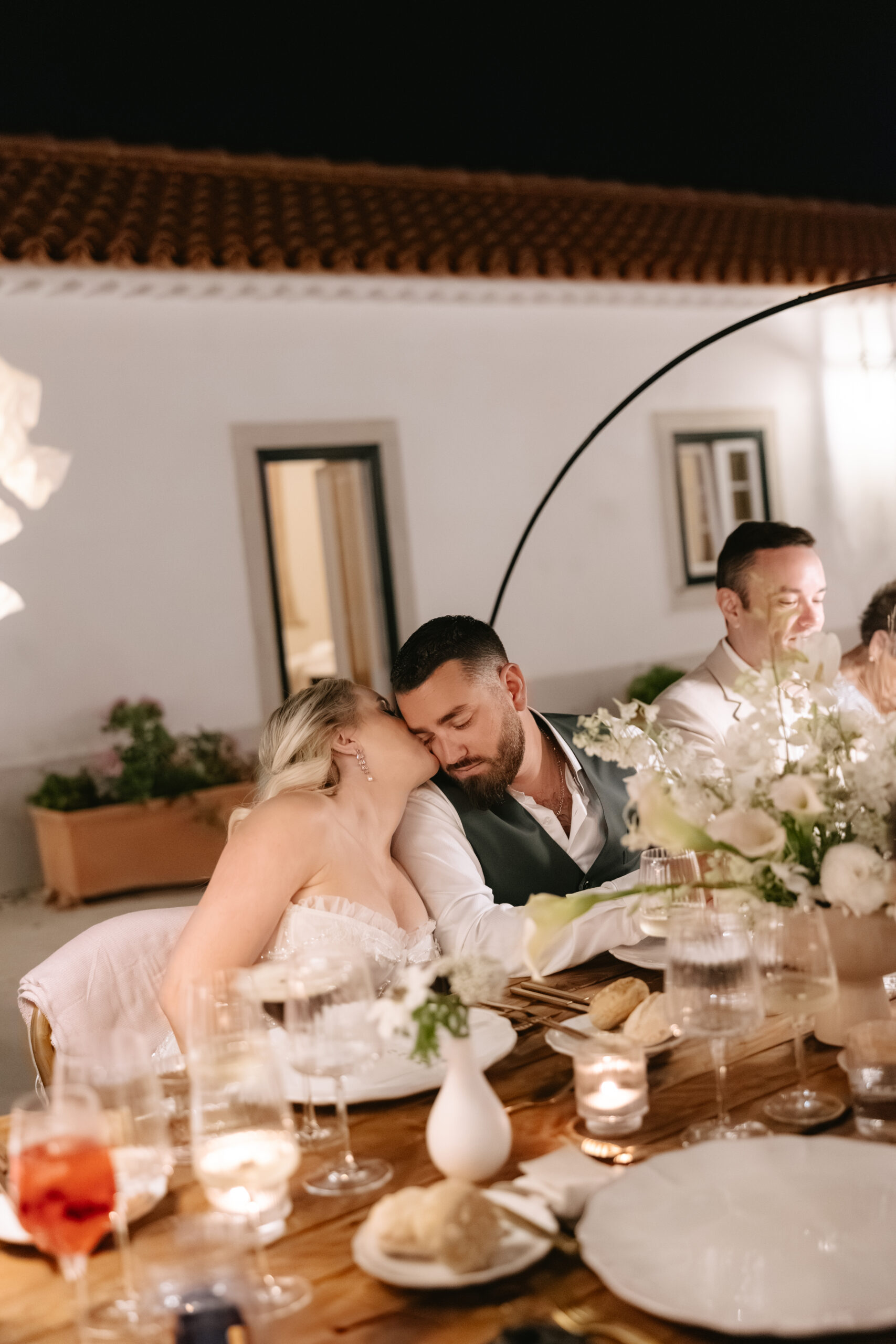 Candid wedding photo of bride kissing groom on the cheek at dinner