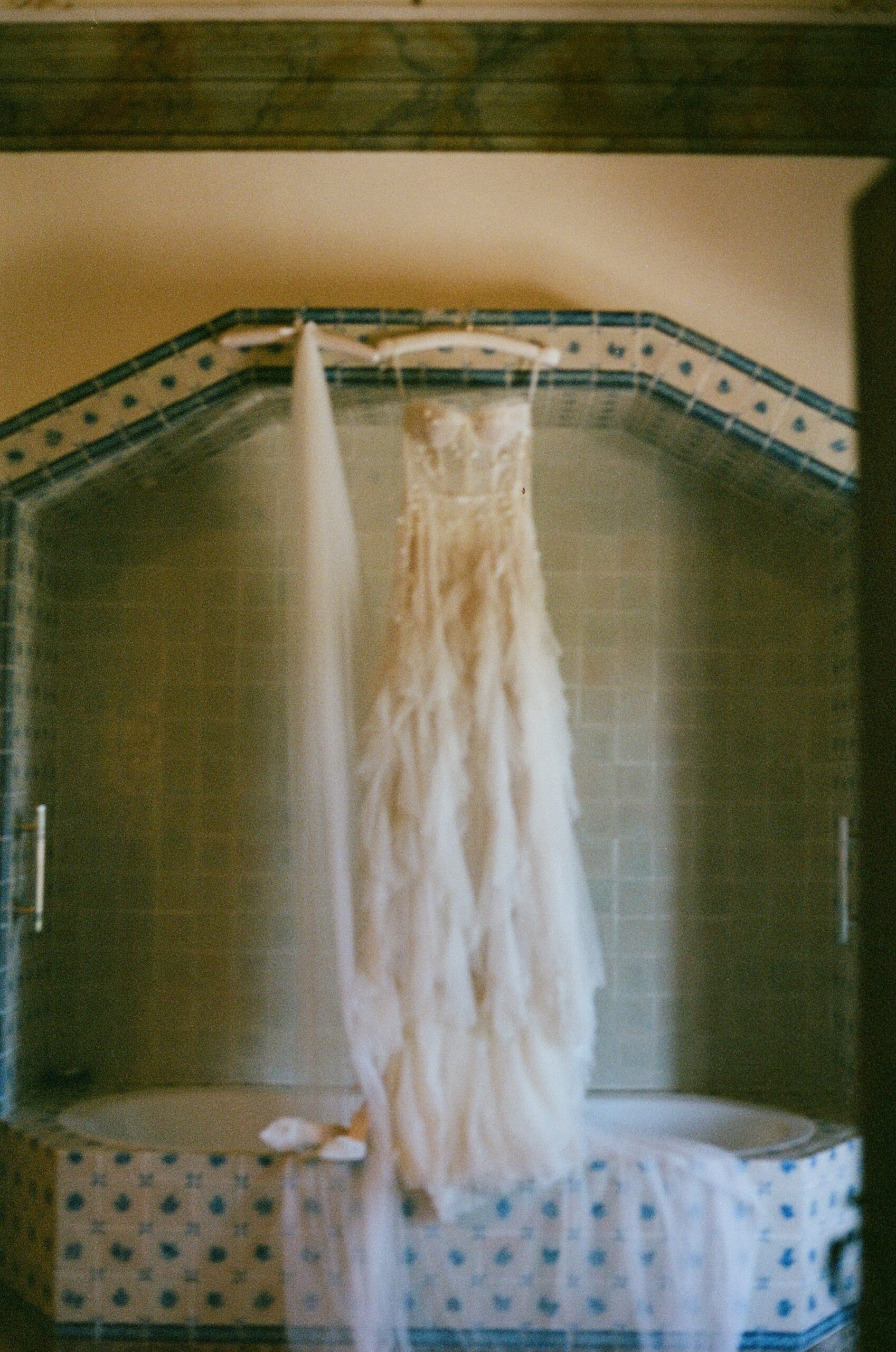 Film wedding photo of wedding dress hanging up in the venue bathroom