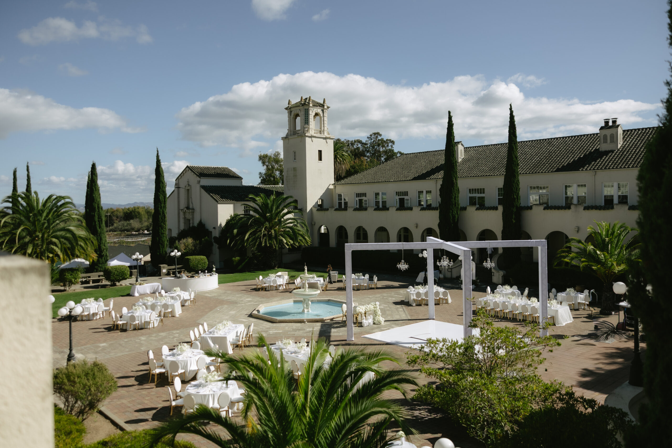 A courtyard set up for a Catholic wedding, with all white tables and a European-inspired building