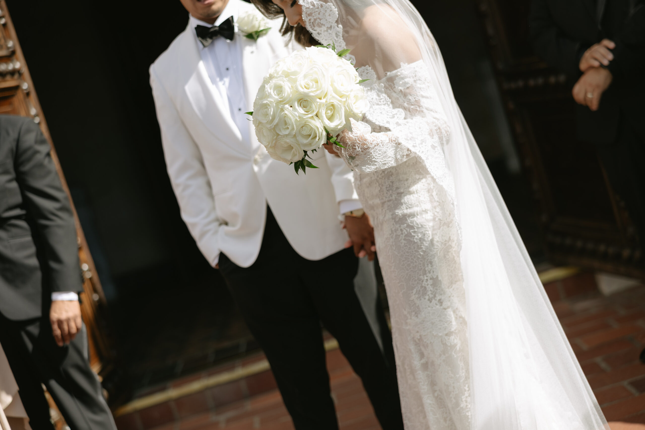 An editorial wedding photo of a bride's lace wedding dress and veil and groom's black and white suit