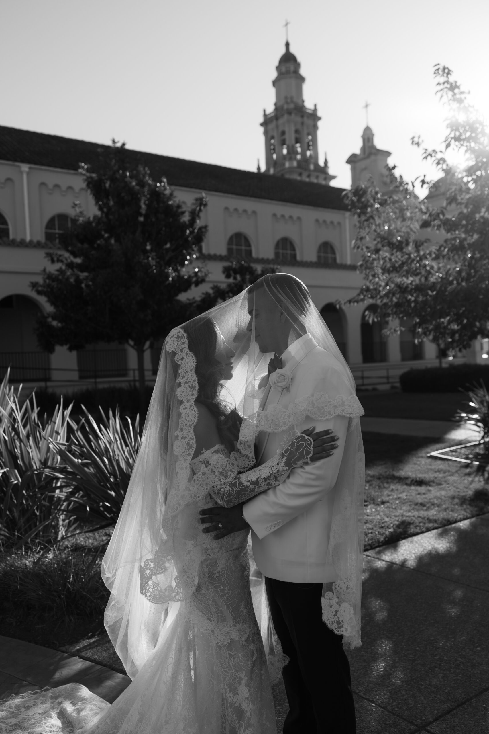 A black and white photo of a bride and groom under a veil