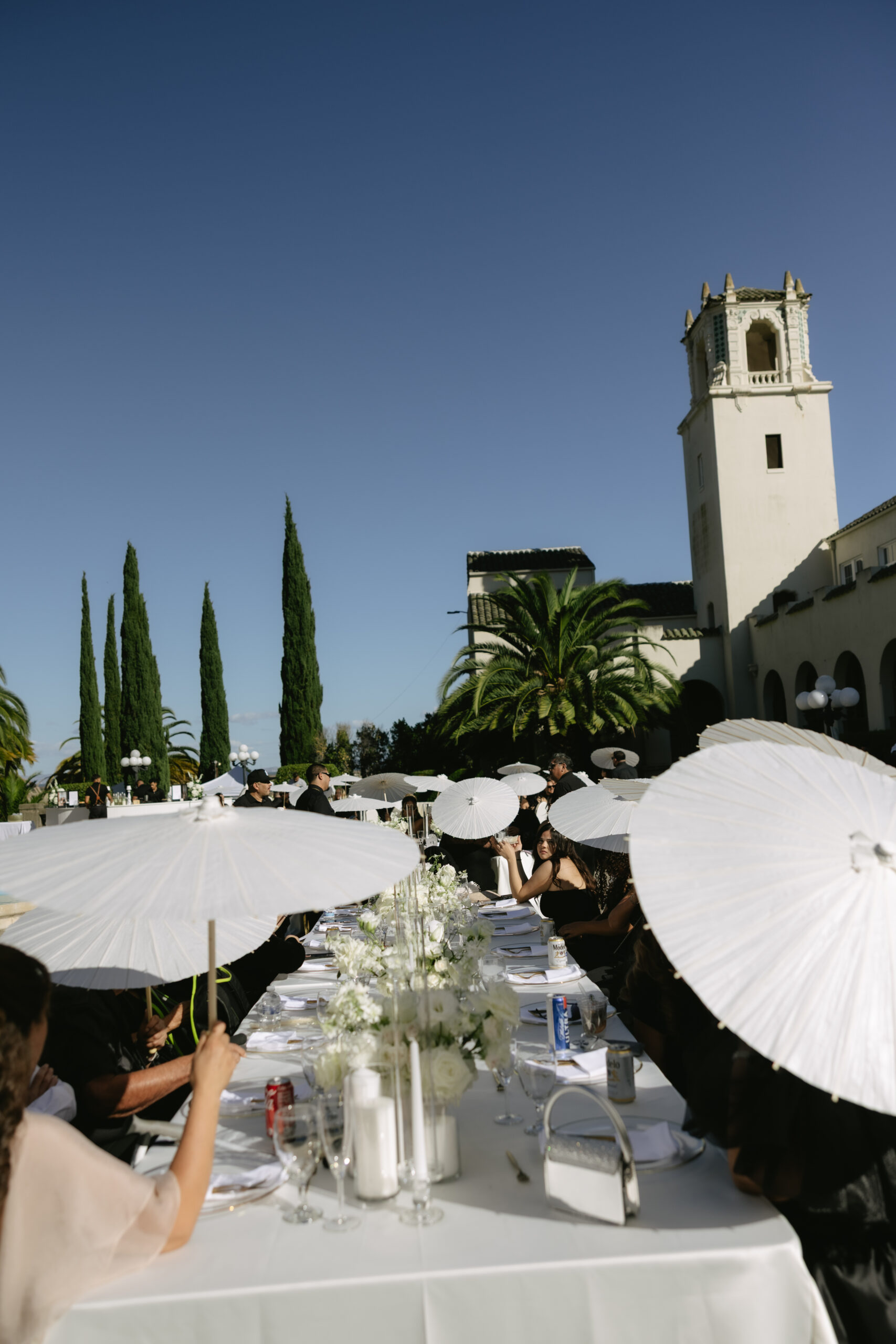 A photo of wedding guests sitting at a wedding table underneath parasols