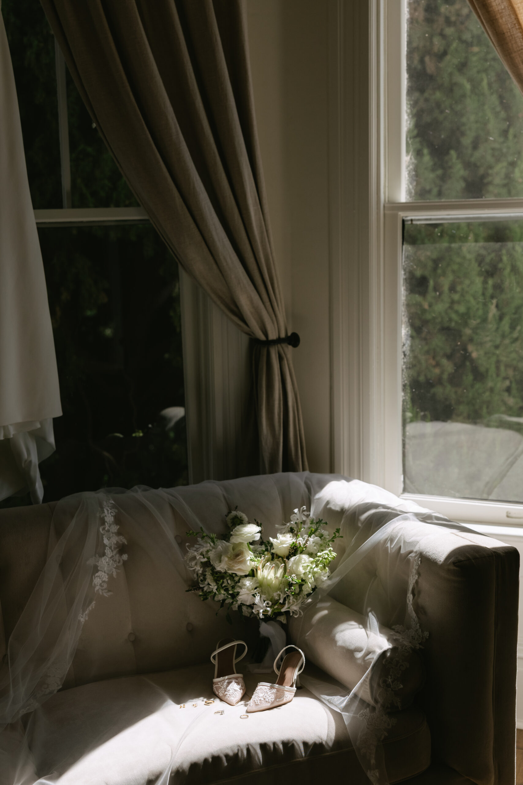 A bride's shoes, veil, and bouquet laying on a couch