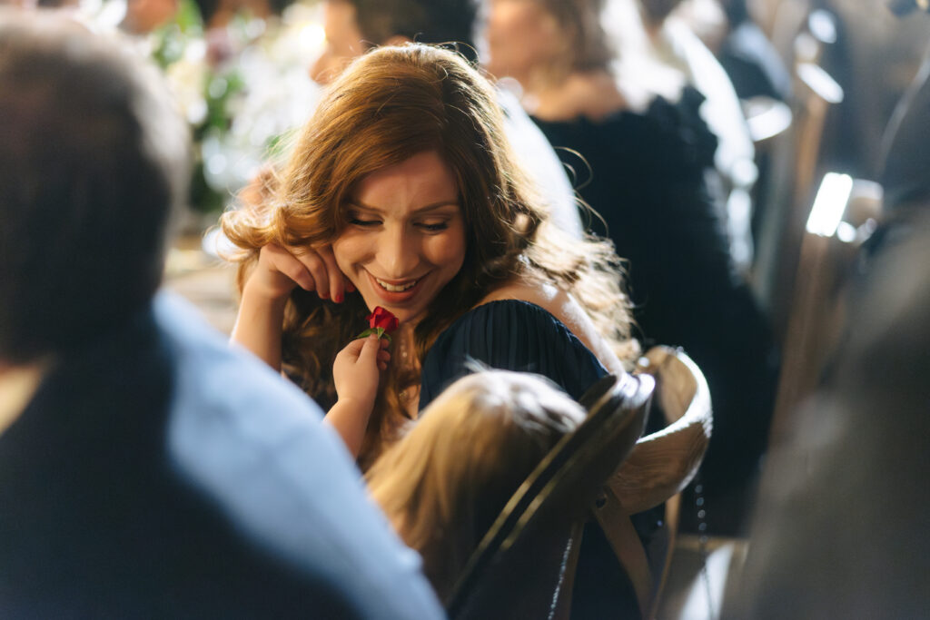 A child holding up a flower to a wedding guest's face during a reception