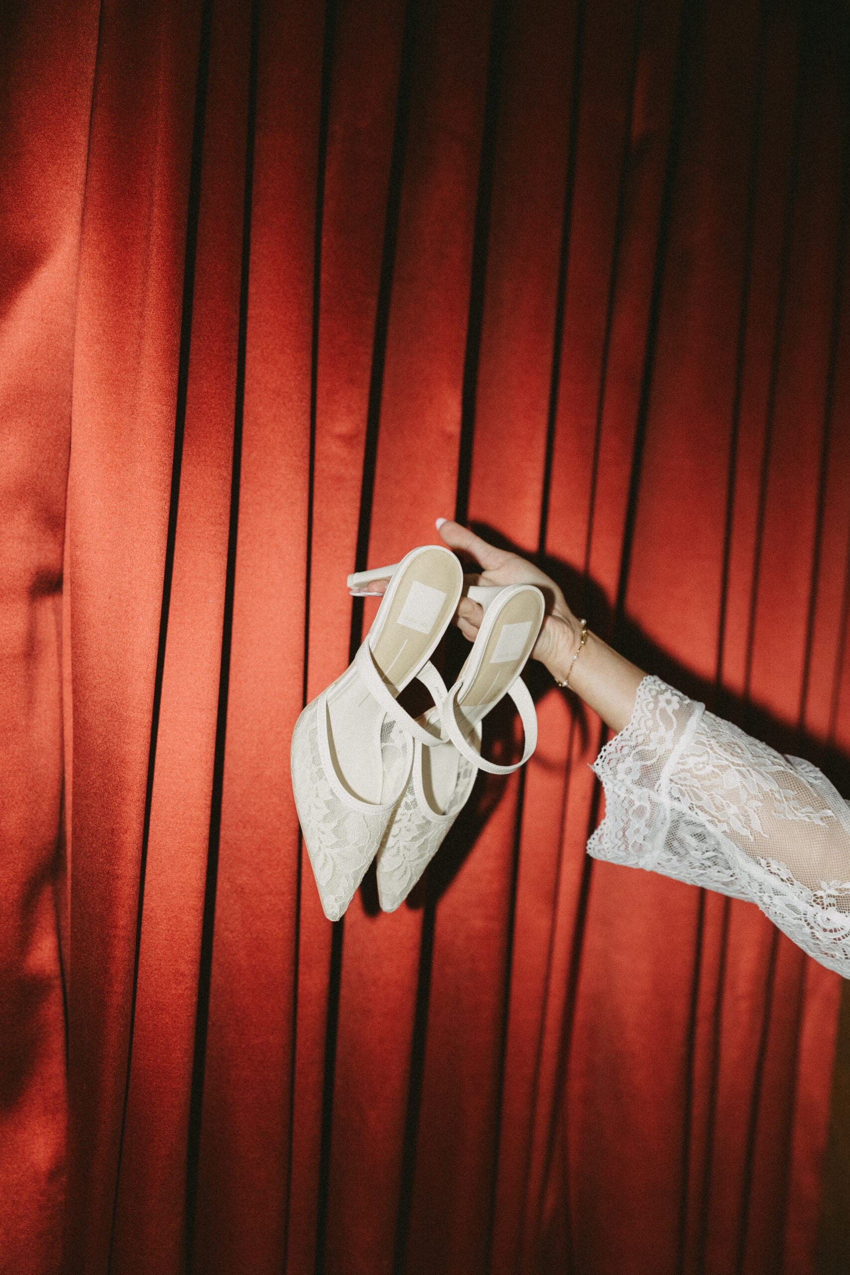 A pair of wedding shoes being held in front of a red curtain