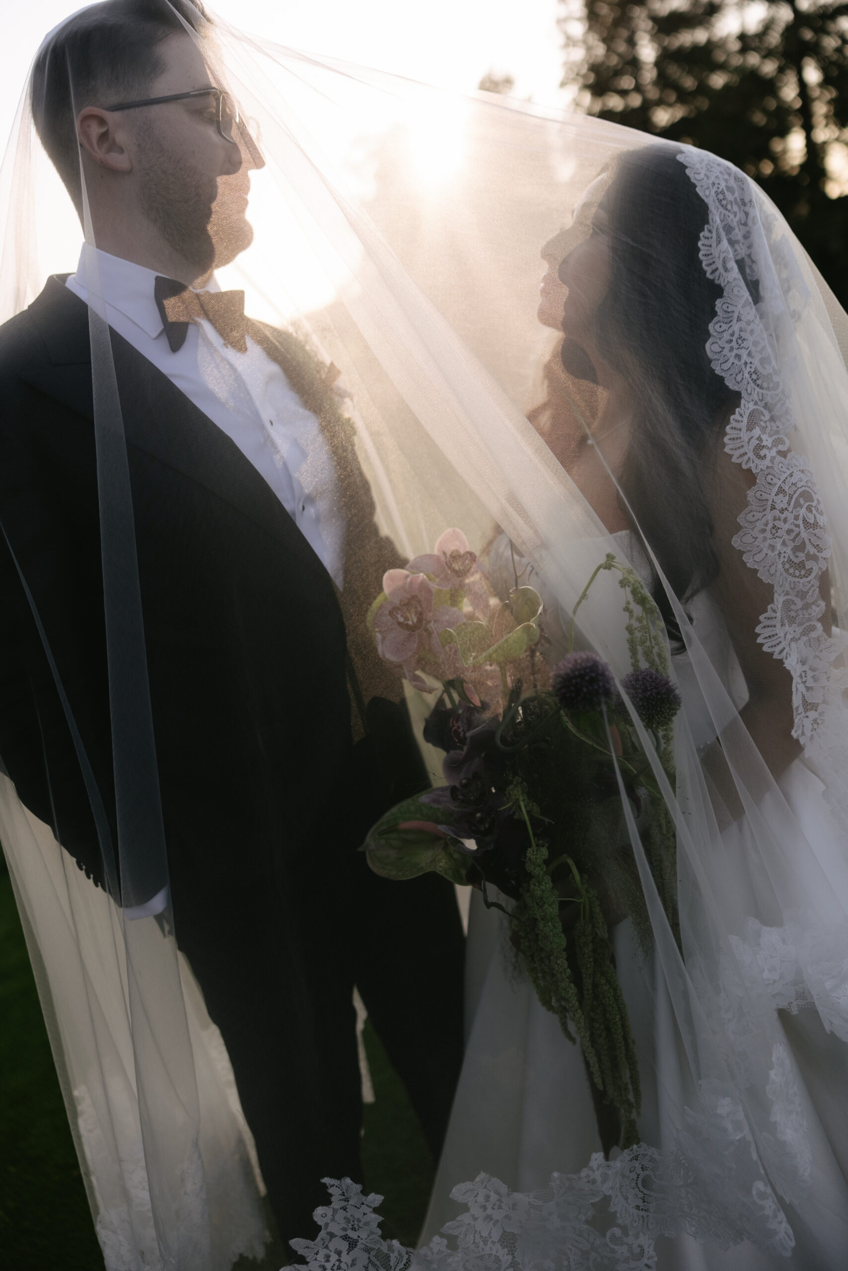 a bride and groom taking wedding photos underneath the bride's wedding veil