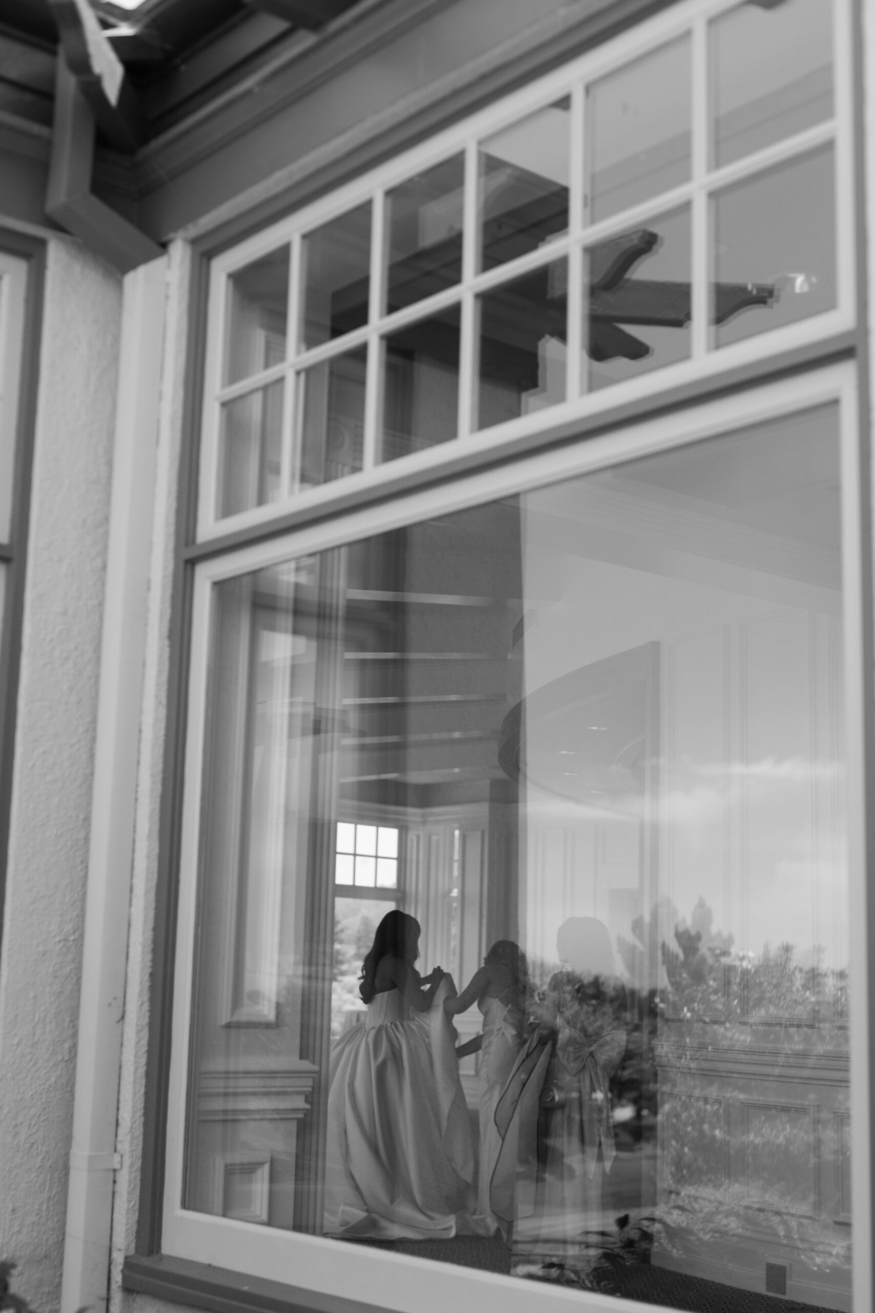Bridesmaids helping a bride get ready, documented through a window by a California wedding photographer